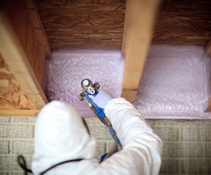 Man installing spray foam insulation in basement box sills.