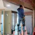 Worker on stilts installing batt insulation.