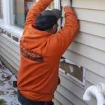Worker assessing the exterior siding around a window.