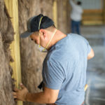Workers installing insulation in the wall of a commercial space.