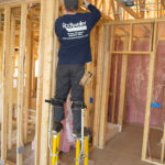 Worker on stilts installing fiberglass batts.