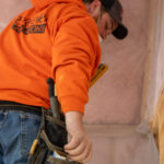 Worker installing wall batts, reaching for a tool in his belt.