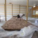 Worker measuring a big piece of insulation on the floor of a large commercial space.