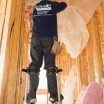 Worker on stilts preparing a new home interior for batt installation.