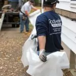 Workers outside a home preparing sidewall insulation.
