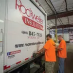 Two workers opening a company truck in a warehouse.