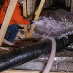 Worker installing blown-in insulation in an attic.