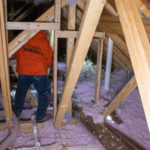 Worker installing blown-in insulation in an attic.