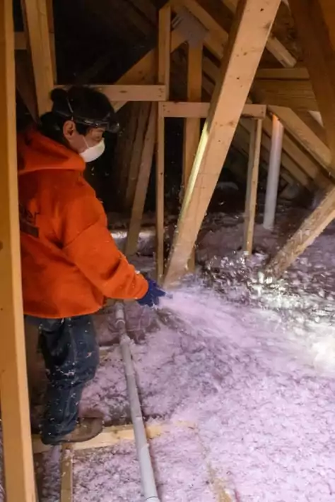 Worker spraying insulation in an attic