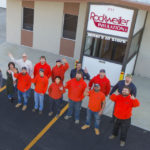 Rockweiler team looking up and waving in front of a company sign.