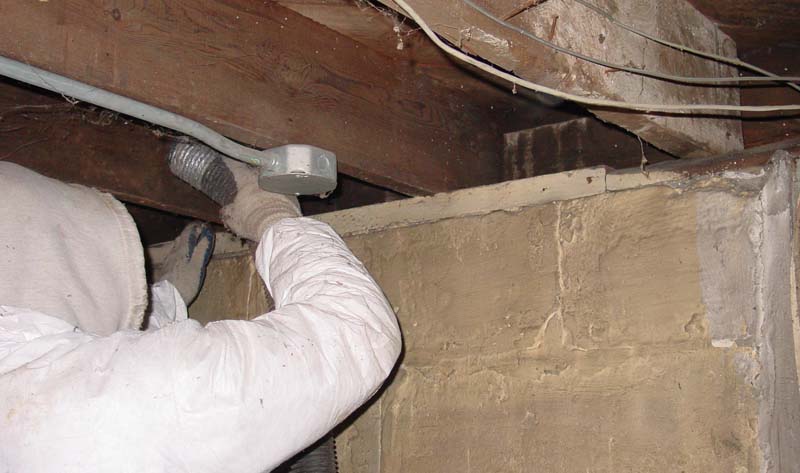 Rockweiler technician spraying foam insulation into a basement rim-joist cavity to air-seal and insulate the box-sill area.