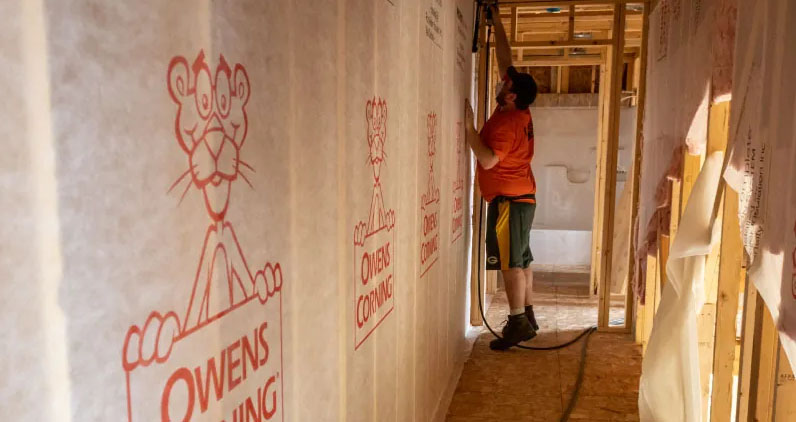 Rockweiler Insulation installer staples Owens Corning Pink Panther-branded mesh to new-construction wall studs, preparing the cavity for blown-in fiberglass insulation.