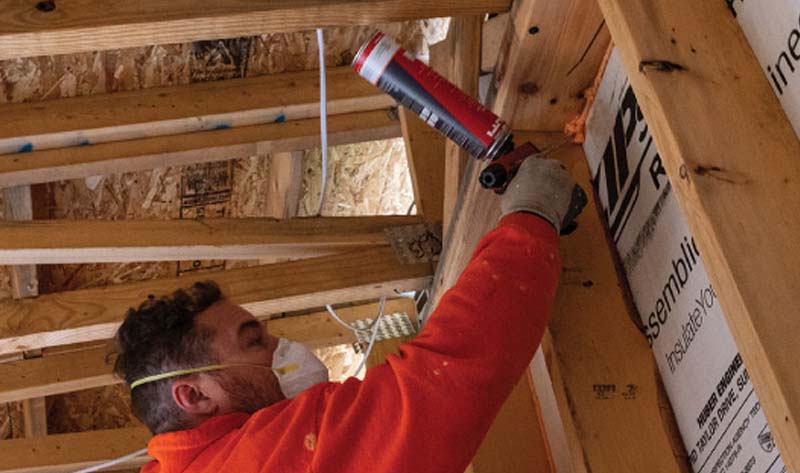 Rockweiler Insulation worker applying spray foam at the top corner of a framed wall inside a residential build.