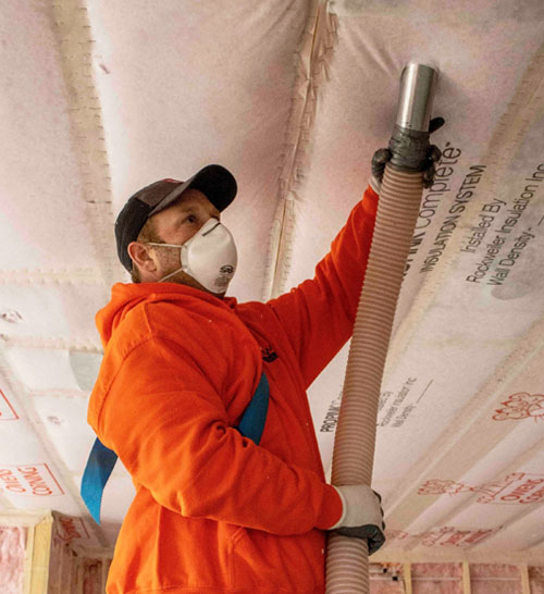 Installer wearing protective gear applies blown-in cellulose insulation to an attic ceiling cavity during a Rockweiler Insulation project in Madison, Wisconsin.