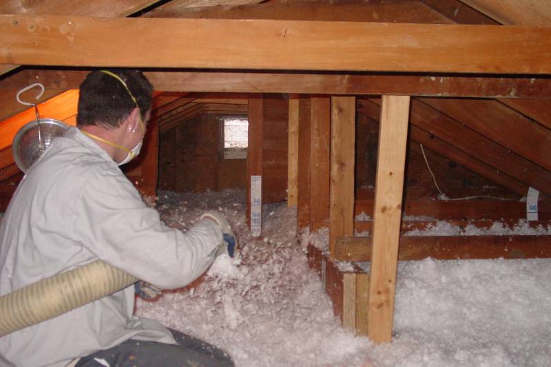 Worker blowing loose-fill insulation in an attic wearing a respirator mask.
