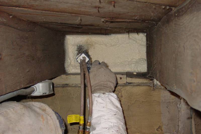 Technician applying spray foam to seal a basement rim joist cavity.