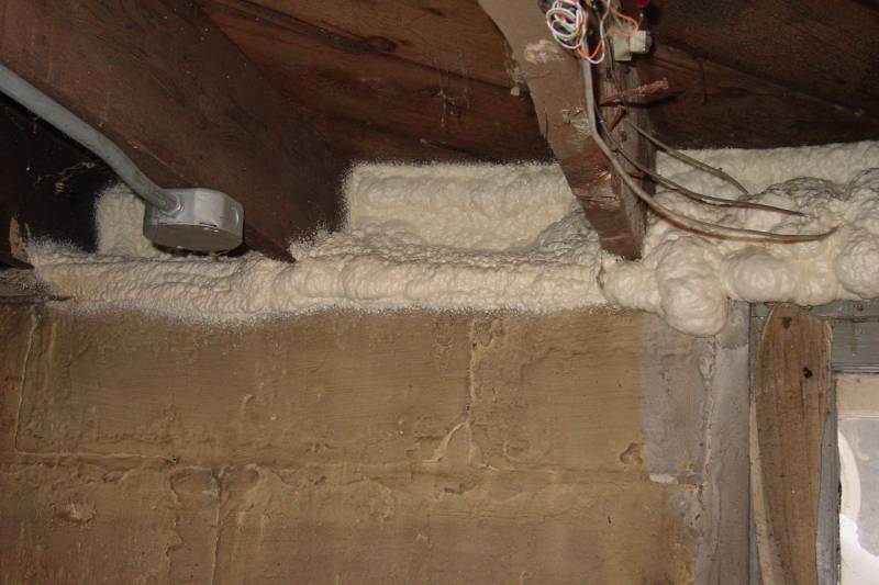 Spray foam insulation applied along a basement sill plate and rim joist.