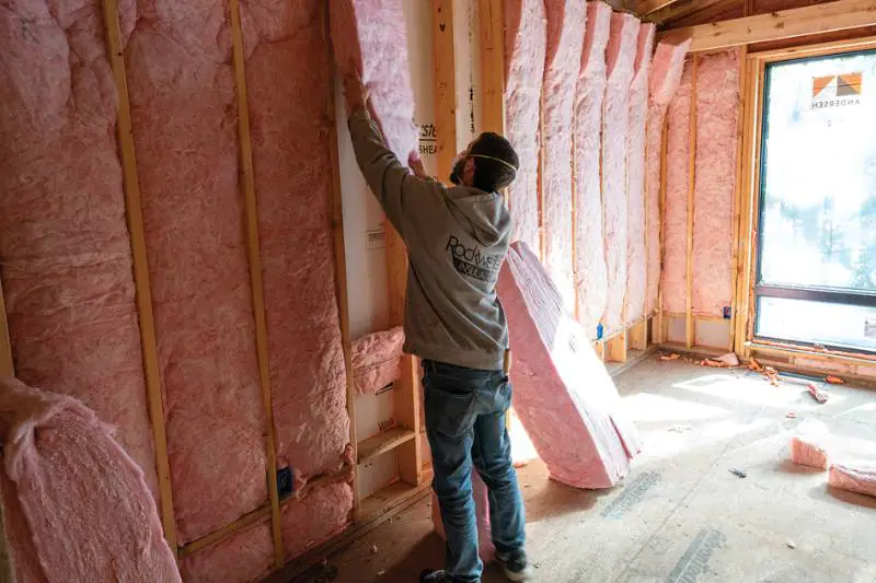 Rockweiler Insulation worker placing a large pink batt into a framed wall cavity.