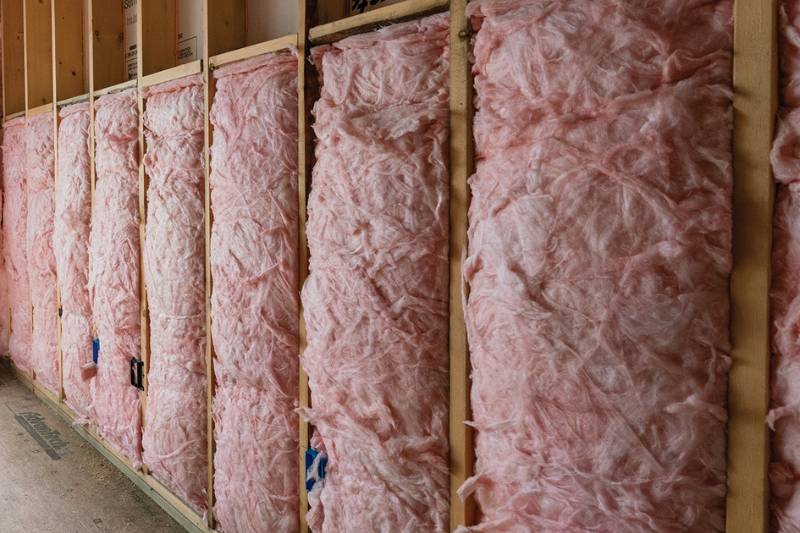Pink fiberglass batt insulation filling wood-framed wall cavities.